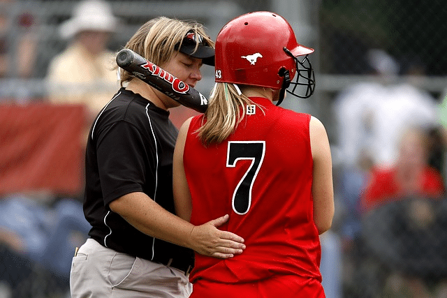 Le coach accompagne et supporte, mais c'est au joueur de briller ! (une coach encourage une joueuse de baseball).